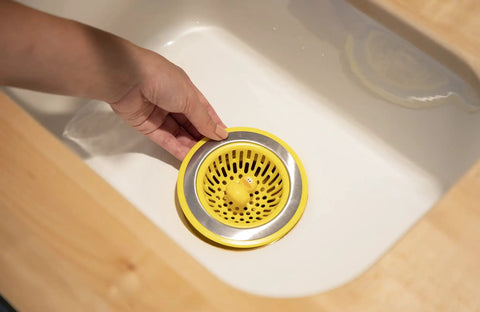 Hand placing Quack Duck Kitchen Sink Strainer Basket Fits All Standard Sinks 4 And A Half Inch Stainless Steel Drain Cover With Bright Yellow Duck Design