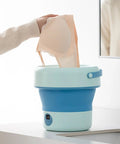 Hand placing delicate items into a Foldable Mini Washing Machine 4.8 Liter Portable Compact Laundry Soaker for quick rinse.