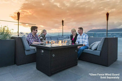 44 Inch Outdoor Propane Fire Pit Table With 50,000 BTU Heat, tempered glass top, used by a group sitting on a patio at sunset.