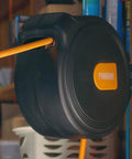 Compact Retractable Air Hose Reel With Brass Fittings And Mounting Bracket One Quarter Inch By Sixty Five Feet Spring Powered Lead Hose Included Durable Hybrid PVC Hose For Easy Shop Or Garage Air Access mounted on a garage wall