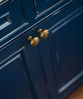 Real Deal Antique Brass Cabinet Knobs 1 1/4 Inch Round Sunburst Design on dark blue cabinet doors.