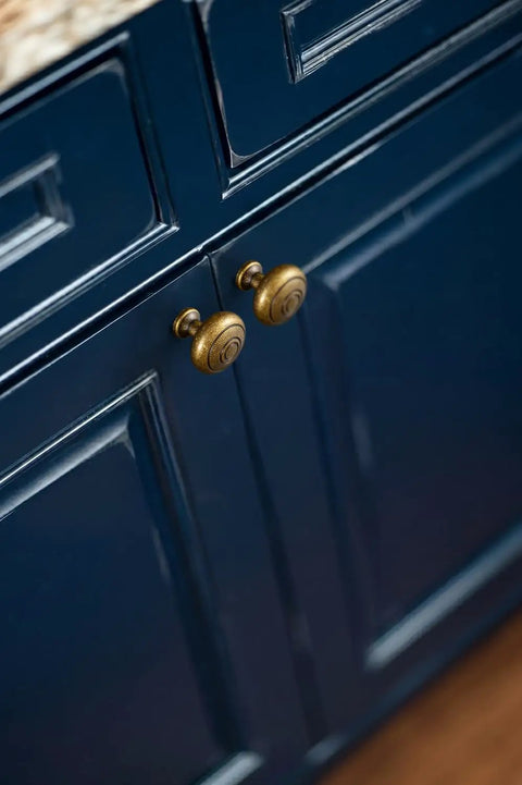 Real Deal Antique Brass Cabinet Knobs 1 1/4 Inch Round Sunburst Design on dark blue cabinet doors.