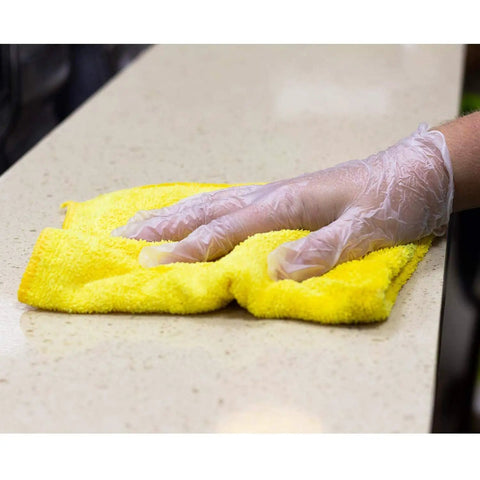 Hand wearing Large 1000 Count Clear Vinyl Disposable Gloves Powder Free Great Fit on yellow cloth for janitorial use