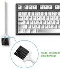 Keyboard cleaning brush with white handle and black bristles beside a mechanical keyboard; close-up of bristles