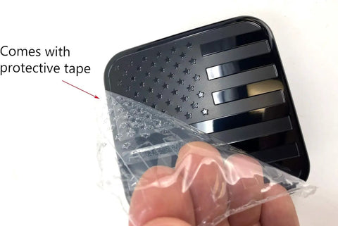 Black Metal Flag Trailer Hitch Cover For 2 Inch Receivers with protective tape being removed, patriotic flag design visible