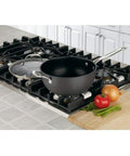 Chef's Classic Nonstick Hard Anodized 4-Quart Pan With Helper Handle And Glass Lid on stovetop beside vegetables.
