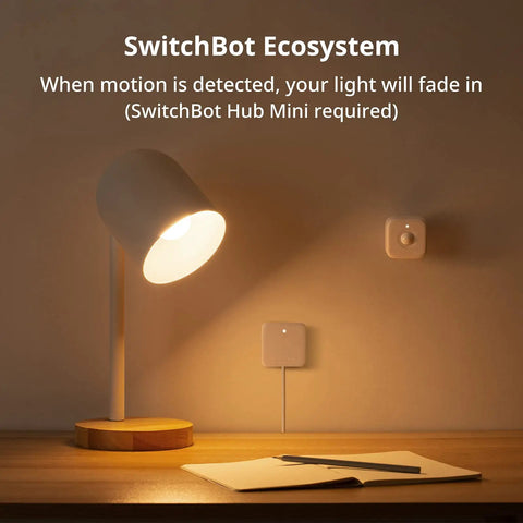 Smart LED Light Bulb illuminating desk in SwitchBot ecosystem setup with motion sensors on wall, cozy home setting.
