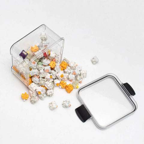 Front view of a clear plastic keyboard switch storage box with lid, 460ml capacity, spilled white and orange switches.