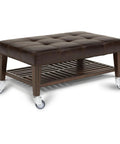 Brown tufted leather ottoman with wooden frame and four caster wheels; lower slatted shelf.