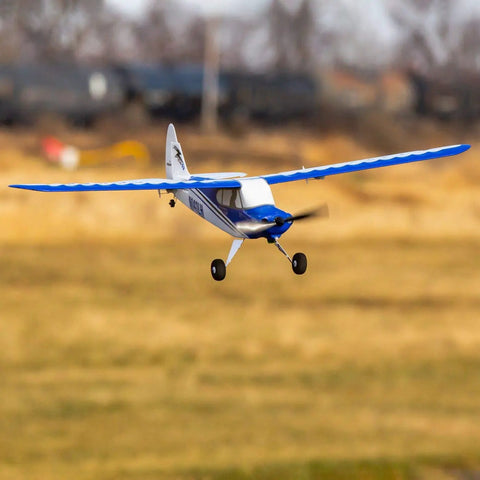 Blue and white Sport Cub S 2 RC Airplane BNF Basic with safe technology flying outdoors on a grassy field