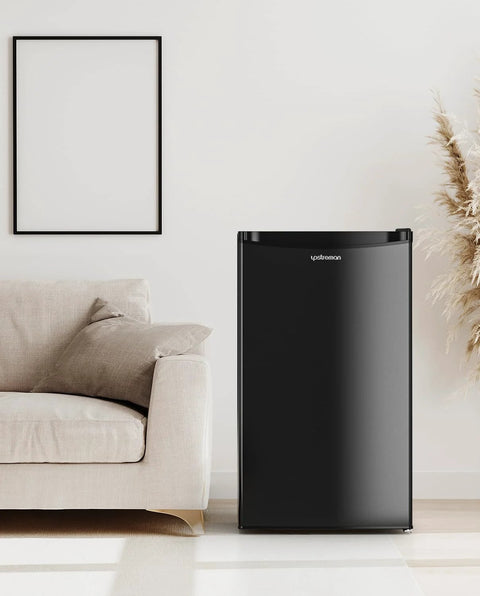 Front view of Upstreman 3.2 cu ft black single-door mini fridge with freezer beside a beige sofa in a living room.
