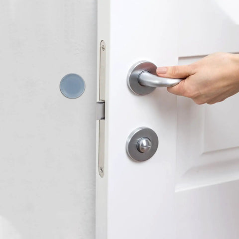 Close-up of a hand gripping a silver door handle on a white door with a blue furniture slider for protection.