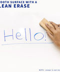 Person erasing blue marker text on Super Smooth White Corner Standing Desk With Dry Erase Surface L Shaped Sit Stand Workstation.