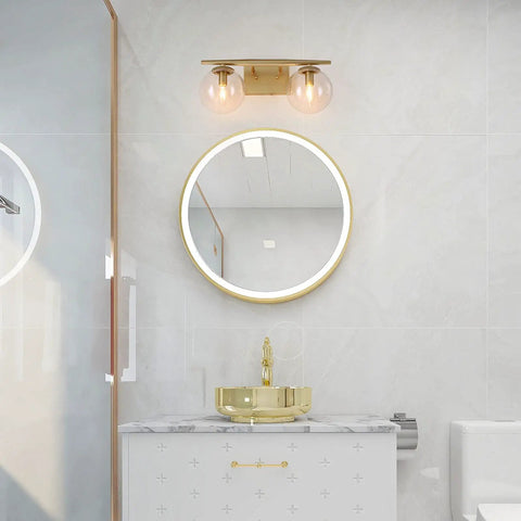 Gold Vanity Light 2-Light Fixture With Globe Clear Glass Shades For Bathroom, mounted above round mirror, premium gold finish.