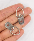 Close-up of two silver steel D-ring picture hangers held in fingers, part of 100 Pack D Ring Picture Hangers With Screws For Hanging Frames Mirrors Clocks Paintings Ten Pound Load Support One And A Quarter Inch Long Five Eighths Inch Wide Bulk Pack Includes 100 Six By One Half Inch Slotted Phillips Combo Screws.