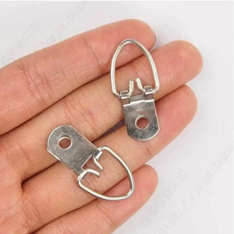 Close-up of two silver steel D-ring picture hangers held in fingers, part of 100 Pack D Ring Picture Hangers With Screws For Hanging Frames Mirrors Clocks Paintings Ten Pound Load Support One And A Quarter Inch Long Five Eighths Inch Wide Bulk Pack Includes 100 Six By One Half Inch Slotted Phillips Combo Screws.