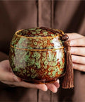 Kick Up Your Pantry Game With These Premium Ceramic Sealed Storage Jars For Loose Tea And Coffee Beans Featuring Ridiculously Tight Lids Really Cool Retro Double Bin Gift Box Organizer, close-up of green and brown ceramic jar with tassel.