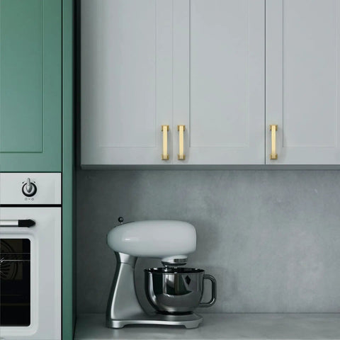 Modern kitchen with white cabinets and gold handles next to a green unit with a mixer on the countertop.