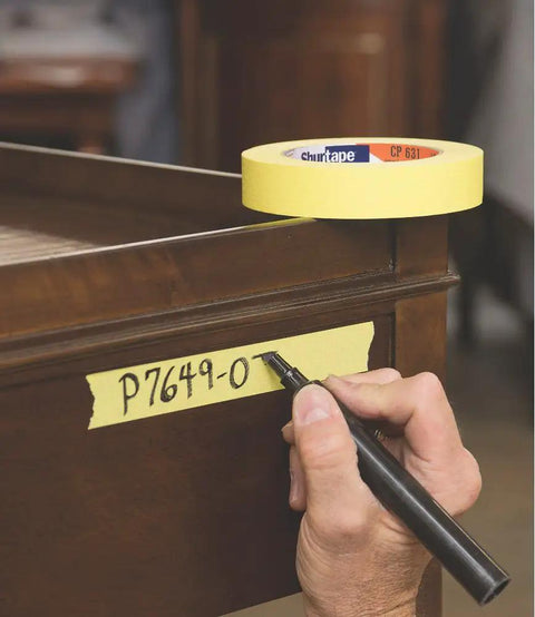 Person writing on CP 631 General Purpose Masking Tape 24mm x 55m White With Medium-High Adhesion, used for labeling on wooden surface.