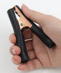 Hand holding black copper Beefy Insulated Alligator Clips Kit, 100 Amp Heavy Duty Jumper Clamps For Cars, Boats, And Batteries