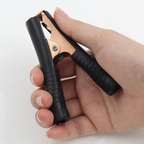 Hand holding black copper Beefy Insulated Alligator Clips Kit, 100 Amp Heavy Duty Jumper Clamps For Cars, Boats, And Batteries