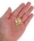 Close-up of FOYTOKI brass foldable cabinet hinge held in hand; small door hardware with four screw holes.