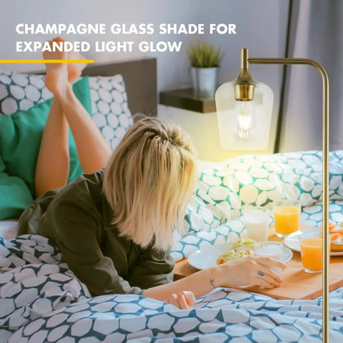 Gold Floor Lamp For Bedroom And Living Room, Industrial Tall Standing Light With Pedal Foot Switch, Farmhouse Modern Style With Champagne Glass Shade, 5.9ft Cord, E26 Bulb Included illuminating a cozy bedroom setting.