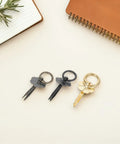 Three multi-tool keyrings in black and gold on a desk with notebook and plant.