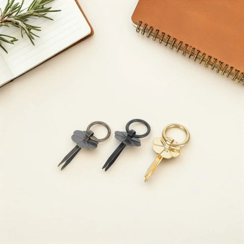 Three multi-tool keyrings in black and gold on a desk with notebook and plant.