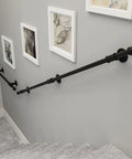 Black Wrought Iron Stair Handrail Wall Mounted Indoor Outdoor Support Bar With Kickass Ergonomic Grip Built Tough For Daily Use Senior Safety Adjustable Length Weather Resistant installed alongside artwork on a gray wall.