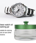 Watch Movement Oil Washing Jar For Repair Pros, glass container with a leak-proof green lid, next to a silver wristwatch.