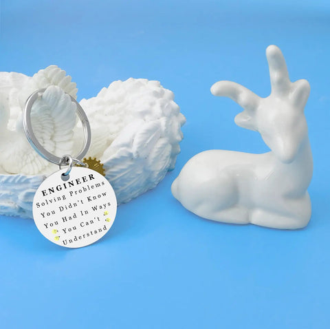 Silver engineering keychain for men with engraved text, next to white ceramic deer, gift for engineers and builders.