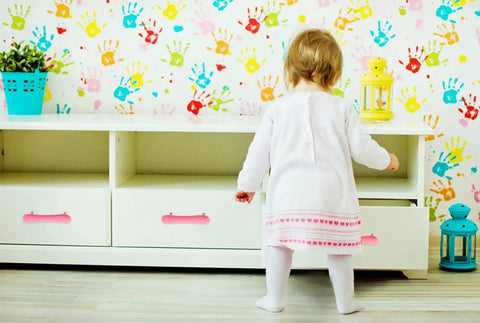 A toddler exploring soft yellow drawer knobs on a white cabinet. Super Cute Soft Rubber Cabinet Handles 5 Inch Long with Zinc Alloy Base Kid Safe Toddler Friendly Drawer Knobs Rust Proof Smooth Finish Yellow Four Pack Includes Installation Screws.