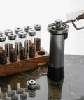 12 Piece Single Dose Coffee Bean Storage Tubes With One Way Exhaust Valve Glass Vials On Sturdy Walnut Wood Base And Easy Pouring Funnel with coffee beans in tubes.