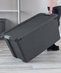 Person carrying Hella Tough 12 Pack 45 Gallon Wheeled Latch Tote plastic storage bin with smooth rolling wheels indoors.