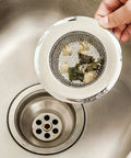 Hand holding Set Of 2 4.5 Inch Diameter Stainless Steel Kitchen Sink Basket Strainer with food particles near sink drain