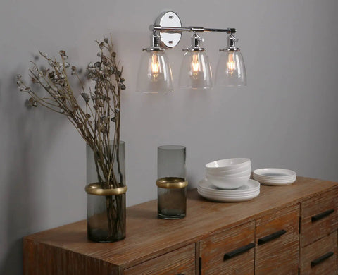 Three Light Industrial Wall Sconce With On Off Switch And Clear Glass Shade For A Cool Retro Vibe Vintage Antique Brass Vanity Lighting For Bathroom And Living Room Dimmable When Paired With A Compatible Dimmer Bell Shade Finish illuminated above wood cabinet