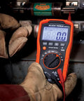 Digital Auto Ranging Multimeter For AC DC Voltage And Current With Temperature Frequency Capacitance Duty Cycle Diode And Continuity Tests 1000V CAT IV 600V CAT III 1000V Safety Built Tough And Drop Ready Orange in use by technician.