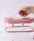 Hand holding a pink transparent waterproof makeup bag from Two Pack Transparent Waterproof Makeup Bag Set With Zippered Cosmetic Pouches For Travel Grab And Go Easy Access Clear PVC Toiletry Organizer Durable Portable Storage Eight Point Three By Five Point Nine By Three Point Five Inch Pink And Green.