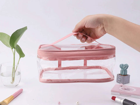 Hand holding a pink transparent waterproof makeup bag from Two Pack Transparent Waterproof Makeup Bag Set With Zippered Cosmetic Pouches For Travel Grab And Go Easy Access Clear PVC Toiletry Organizer Durable Portable Storage Eight Point Three By Five Point Nine By Three Point Five Inch Pink And Green.