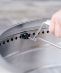 Hand attaching Yukon 27 Inch Fire Pit Handle Accessory for easy portable carry. Locking mechanism details shown.