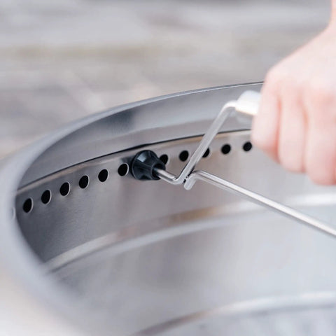 Hand attaching Yukon 27 Inch Fire Pit Handle Accessory for easy portable carry. Locking mechanism details shown.
