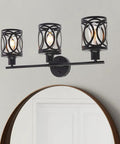 Three Light Industrial Vanity Light Fixture In Black Farmhouse Wall Sconce For Bedroom, Kitchen, Living Room, Bathroom, And Foyer, Vintage Vibe Lighting With E26 Base against a gray wall above a mirror.