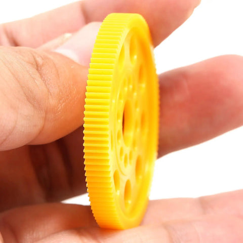 64P 100T Spur Gear For 1 By 10 On Road RC Cars, lightweight yellow plastic gear held in hand, designed for faster acceleration.
