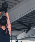 Person lifting a dumbbell under an Industrial Grade 24 Ft HVLS Ceiling Fan With Built In VFD Brushless Motor And Remote Control.