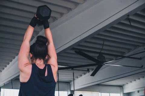 Person lifting a dumbbell under an Industrial Grade 24 Ft HVLS Ceiling Fan With Built In VFD Brushless Motor And Remote Control.