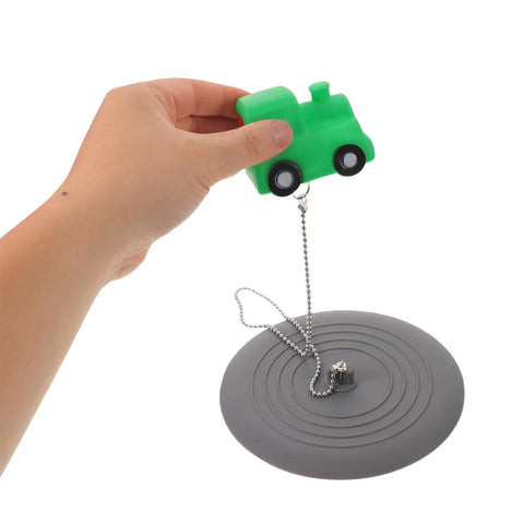 Hand holding a green train toy above TEHAUX Silicone Bathtub Drain Stopper 15cm, Hair Catcher for Bathroom.