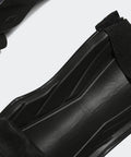 Close-up of Youth Shin Guards For Soft Ground Soccer Tiro Shield With EVA Backed Protection One Strap Quick Adjust Fit Ankle Sleeve Guard in black.