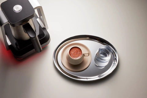 Top view of Turkish Coffee Maker Electric With Open Form Design For Watching Foam Rise next to a cup of brewed coffee on a tray.