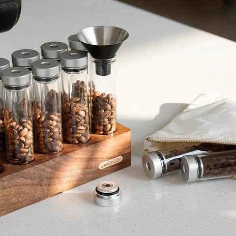 12 Piece Single Dose Coffee Bean Storage Tubes With One Way Exhaust Valve Glass Vials On Sturdy Walnut Wood Base and Easy Pouring Funnel with beans.